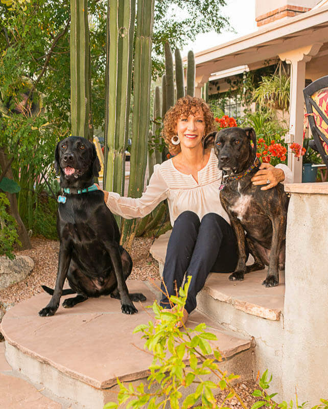A woman with two dogs sitting in a garden full of plants native to Southern Arizona